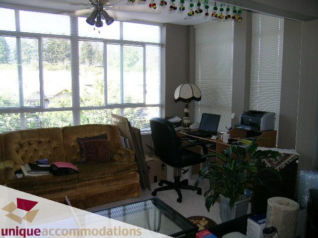 Living room with large windows, couch, desk, and plants. - 314 - 855 W. 16th Street, North Vancouver
