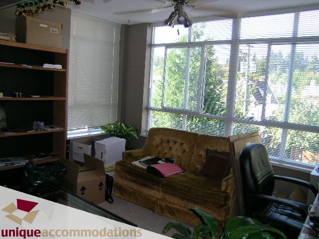 Living room with large windows, greenery outside, and a brown armchair. - 314 - 855 W. 16th Street, North Vancouver