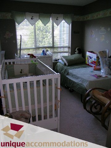 Bright bedroom with white crib, green bedding, and window with blinds. - 314 - 855 W. 16th Street, North Vancouver