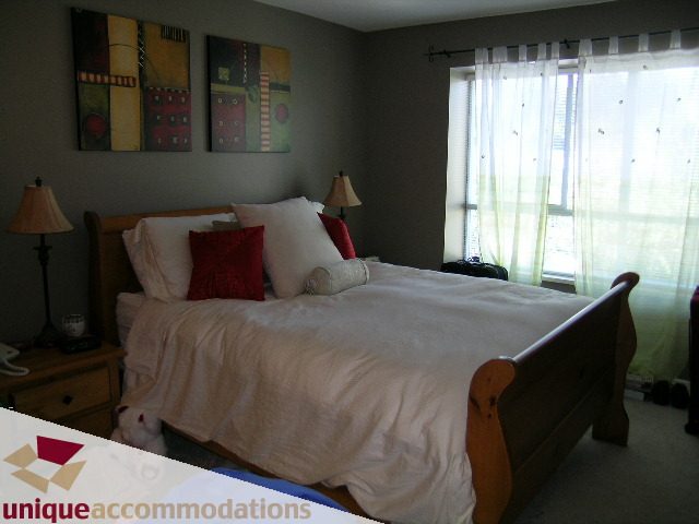 Furnished bedroom with wooden bed, white bedding, and abstract wall art. - 314 - 855 W. 16th Street, North Vancouver