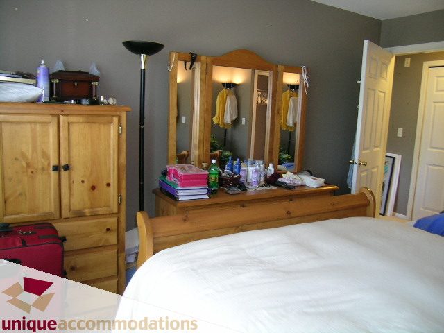Furnished bedroom with wooden furniture, large mirror, and neatly made bed. - 314 - 855 W. 16th Street, North Vancouver
