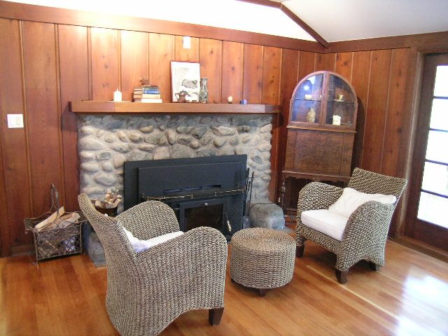 Living room with hardwood floors, stone fireplace, and wicker furniture. - 1250 Seymour Blvd, North Vancouver