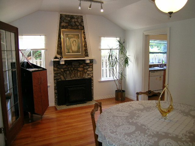 Bright dining area with hardwood floors and a stone fireplace, featuring a patterned tablecloth and a potted plant.
