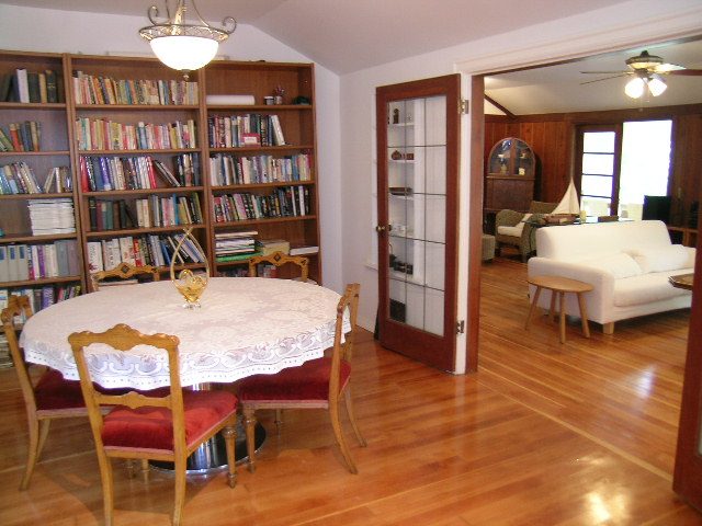 Formal dining area with wooden floors, bookshelves, and a table with red chairs. - 1250 Seymour Blvd, North Vancouver