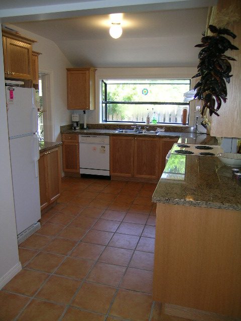 Bright kitchen with terracotta tile floors, granite countertops, and a window view of greenery. - 1250 Seymour Blvd, North Vancouver