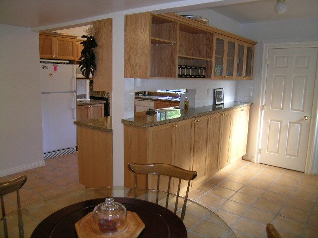 Bright kitchen with wooden cabinets and granite countertops, open to a dining area. - 1250 Seymour Blvd, North Vancouver