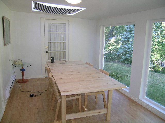 Bright dining area with wooden table and chairs, hardwood floors, and large windows showing greenery. - 1250 Seymour Blvd, North Vancouver