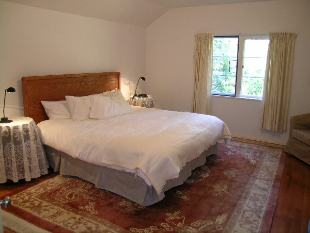 Spacious bedroom with wooden headboard, white bedding, and patterned rug. - 1250 Seymour Blvd, North Vancouver