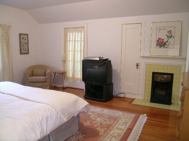 Bright bedroom with hardwood floors, a cozy fireplace, and a comfortable armchair. - 1250 Seymour Blvd, North Vancouver