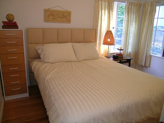 Bright bedroom with striped bedding, wooden floors, and large windows. - 1250 Seymour Blvd, North Vancouver