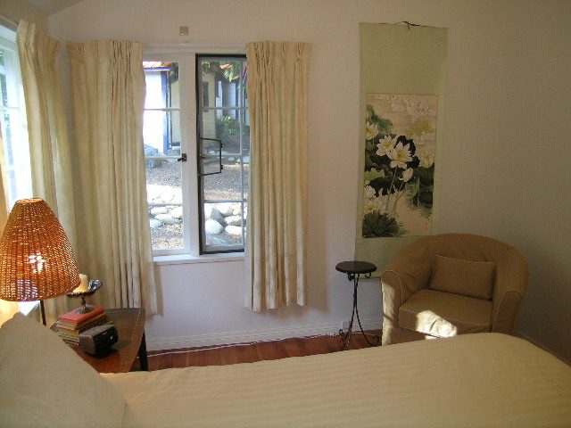 Furnished bedroom with a large window, hardwood floors, and a cozy bed setup. - 1250 Seymour Blvd, North Vancouver