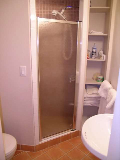 Bathroom with glass shower, neatly arranged towels, and storage shelves. - 1250 Seymour Blvd, North Vancouver