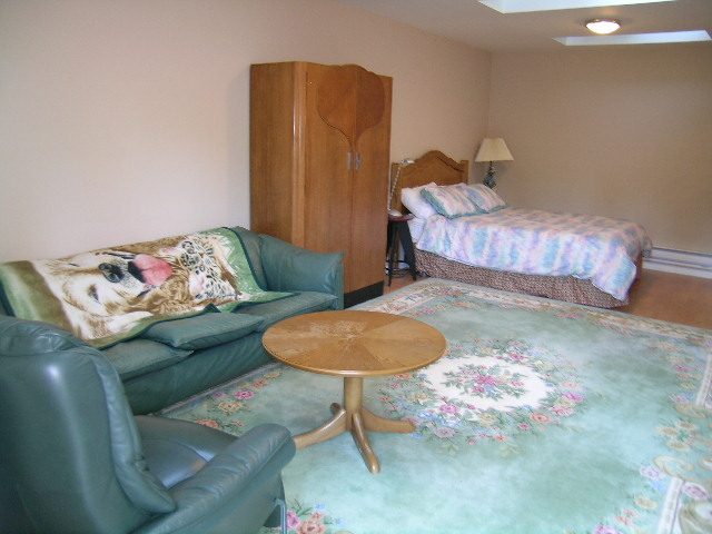 Furnished living room with green leather chairs and floral rug. - 1250 Seymour Blvd, North Vancouver