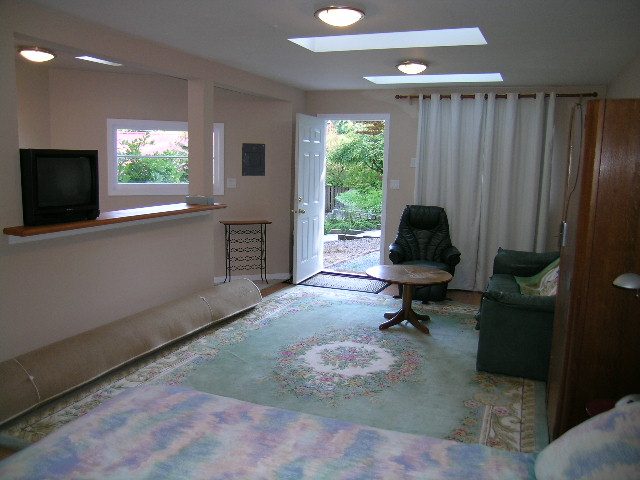 Bright living room with a TV on a shelf and a sliding glass door leading to a patio. - 1250 Seymour Blvd, North Vancouver