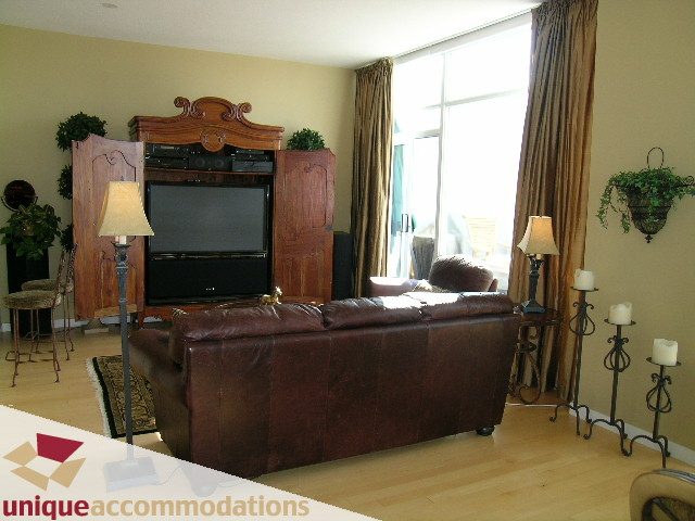 Living room with hardwood floors, large window, and wooden entertainment center. - 3601-193 Aquarius Mews, Vancouver Downtown