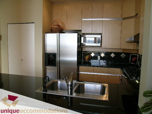 Bright kitchen with stainless steel appliances, black countertops, and light wood cabinets. - 3601-193 Aquarius Mews, Vancouver Downtown