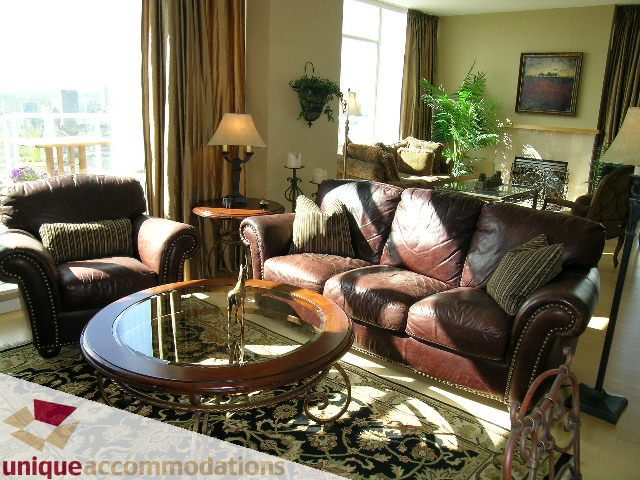 Spacious living room with plush leather furniture, large windows, and city view. - 3601-193 Aquarius Mews, Vancouver Downtown