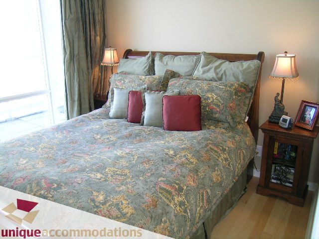 Spacious bedroom with floral bedding, hardwood floors, and a large window with city view. - 3601-193 Aquarius Mews, Vancouver Downtown