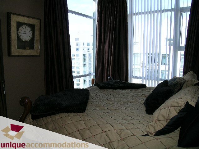 Spacious bedroom with large windows, city view, and cozy bedding. - 3601-193 Aquarius Mews, Vancouver Downtown