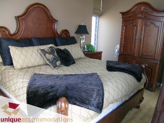 Spacious bedroom with elegant wooden furniture, plush bedding, and a large armoire. - 3601-193 Aquarius Mews, Vancouver Downtown