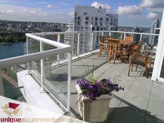 Furnished balcony with city view, wooden furniture, and potted flowers. - 3601-193 Aquarius Mews, Vancouver Downtown