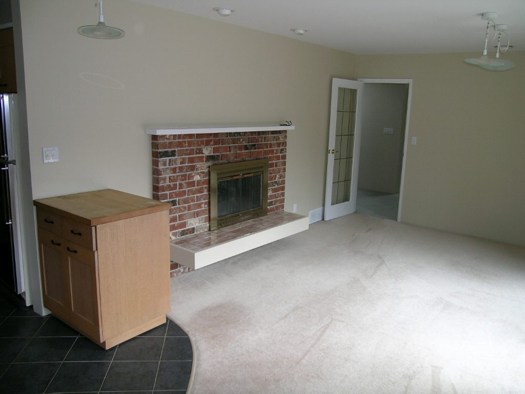 Spacious living room with brick fireplace, light wood cabinets, and neutral carpet. - 2331 Hyannis Drive, North Vancouver