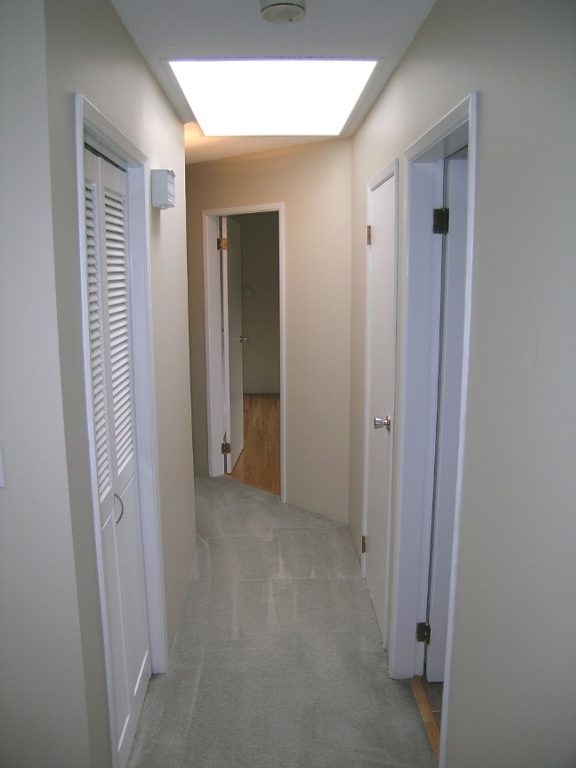 Spacious hallway with light-colored walls, carpeted floor, and white doors leading to bedrooms and a den. - 2331 Hyannis Drive, North Vancouver
