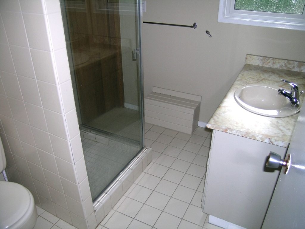Modern bathroom with white tile, glass shower, and marble countertop. - 2331 Hyannis Drive, North Vancouver