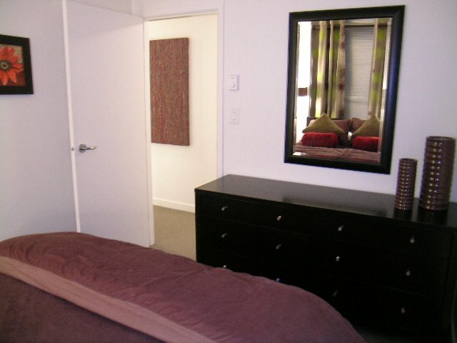 Furnished bedroom with dark wood dresser and large mirror, cozy bedding. - 930 Beatty Street, Vancouver Downtown