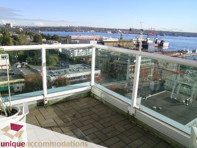 Furnished balcony with glass railings, city view, and harbor in the distance. - PH1 - 125 West 2nd Street, North Vancouver
