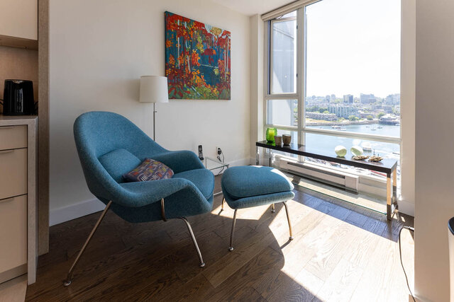 Living room with city view and hardwood floors, featuring a blue chair and vibrant artwork. - 1703-1067 Marinaside Crescent, Vancouver Downtown