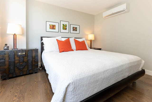 Spacious bedroom with white quilted bed, orange accent pillows, and hardwood floors. - 1703-1067 Marinaside Crescent, Vancouver Downtown