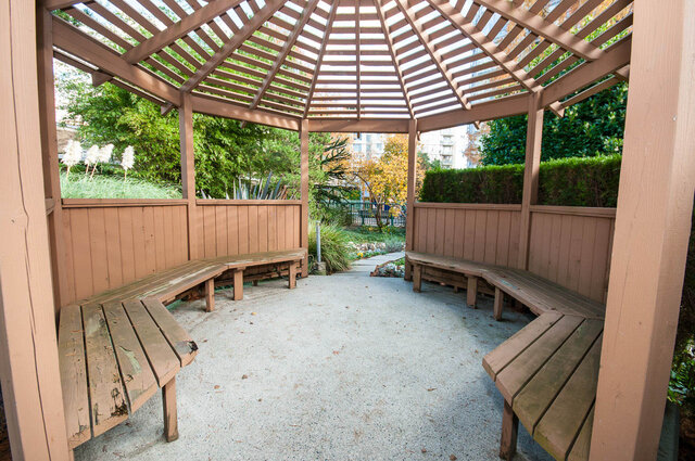 Covered patio with wooden benches and gravel flooring, surrounded by lush greenery. - 1703-1067 Marinaside Crescent, Vancouver Downtown