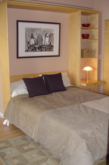 Spacious bedroom with a Murphy bed, wooden shelves, and a cozy bedside lamp. - 403-2228 Marstrand Ave, Vancouver West Side