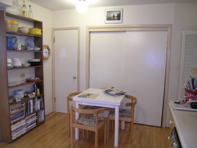 Compact dining area with wooden chairs and a white table, featuring a bookshelf and a sliding door. - 1495 Kings Avenue, West Vancouver