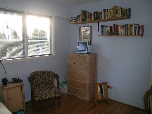 Bright bedroom with hardwood floors, bookshelves, and a cozy chair by the window. - 1495 Kings Avenue, West Vancouver