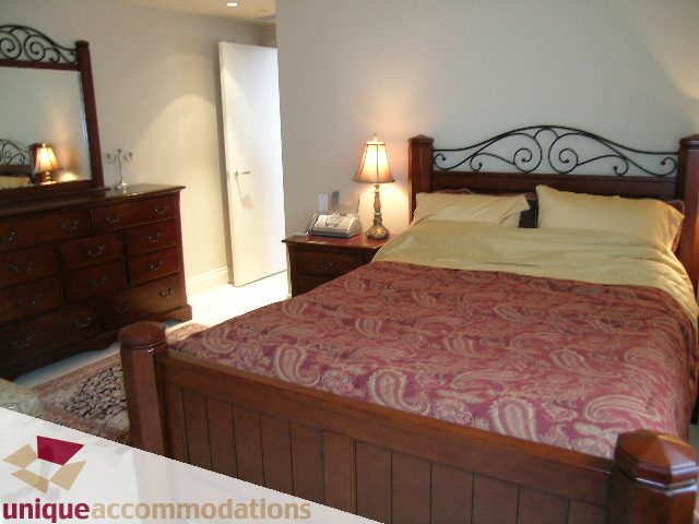 Furnished 2-bedroom condo with wooden furniture, patterned bedding, and a lamp. - 1805 - 428 Beach Crescent, Vancouver Downtown