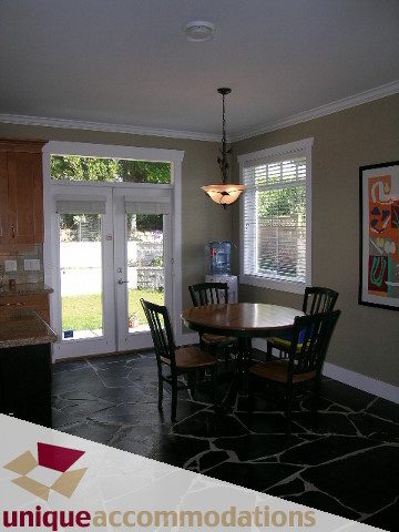 Bright dining area with black stone floors, wooden chairs, and a view of the backyard. - 4330 Canterbury Crescent, North Vancouver