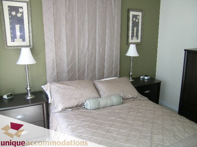 Furnished bedroom with green walls, white curtains, and a neatly made bed with beige bedding. - 945 Homer Street, Vancouver Downtown