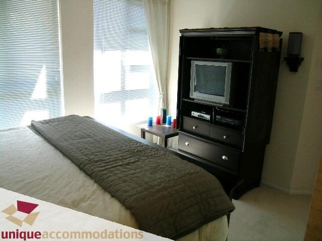 Bright bedroom with a cozy bed, dark furniture, and a window view. - 945 Homer Street, Vancouver Downtown