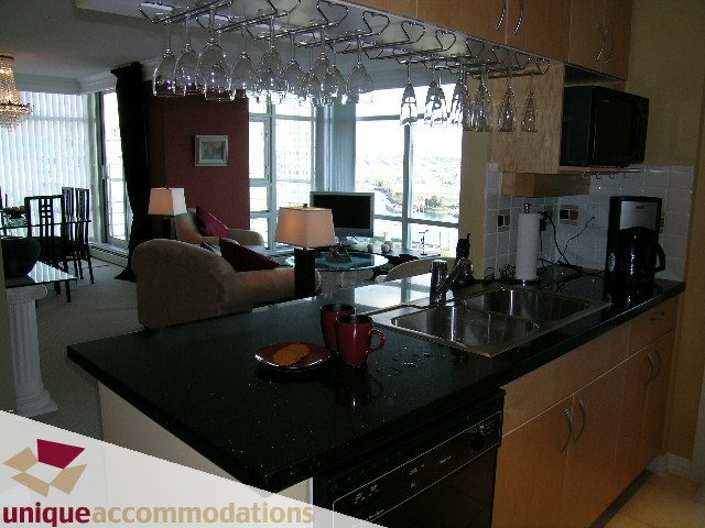Bright kitchen with black countertops, city view, and modern appliances. - 2502 - 1199 Marinaside Crescent, Vancouver Downtown