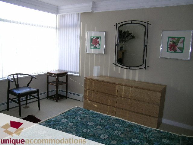 Furnished bedroom with floral bedspread, wooden dresser, and large mirror. - 2502 - 1199 Marinaside Crescent, Vancouver Downtown