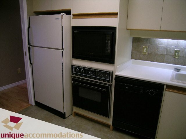 Bright kitchen with white appliances, hardwood floors, and a tiled backsplash. - 105 - 1490 Pennyfarthing, Vancouver West Side
