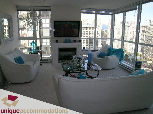 Spacious living room with a city view, modern furniture, and a large TV. - 1904 - 1199 Seymour Street, Vancouver Downtown
