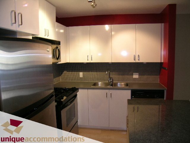 Modern kitchen with sleek stainless steel appliances, white cabinets, and red accents. - 104 - 175 W. 1st. Street, North Vancouver