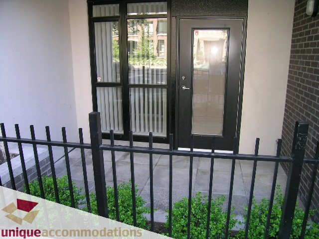 Furnished 1-bedroom + den condo with a cozy balcony, black railings, and a view of the street. - 104 - 175 W. 1st. Street, North Vancouver