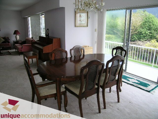 Dining room with wooden table, chairs, and view of greenery outside. - 94 Bonnymuir Drive, West Vancouver