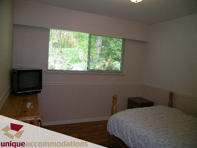 Furnished bedroom with hardwood floors and a view of greenery outside. - 94 Bonnymuir Drive, West Vancouver