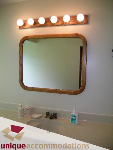Bathroom with wooden-framed mirror and light fixture, clean countertop with toiletries. - 94 Bonnymuir Drive, West Vancouver