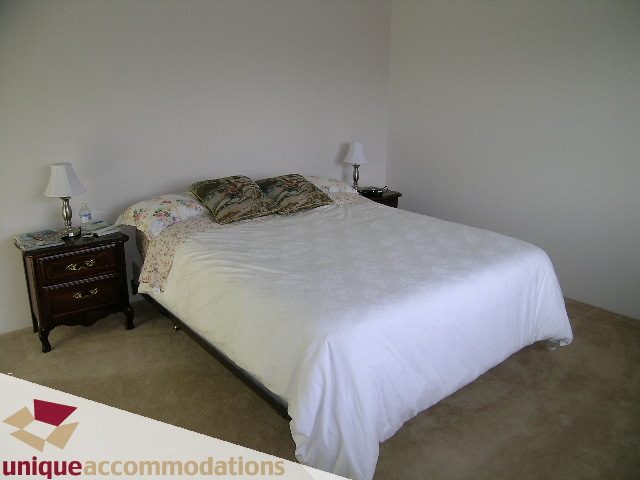 Furnished bedroom with white bedding and patterned pillows, nightstand with lamp. - 94 Bonnymuir Drive, West Vancouver